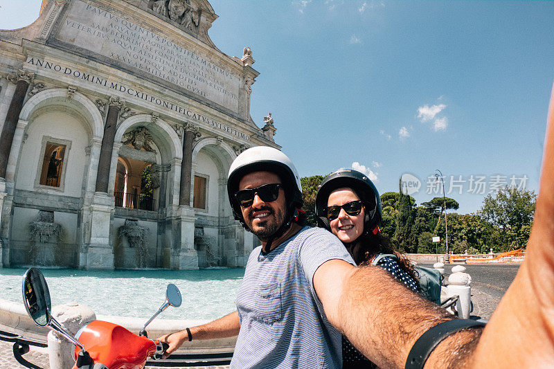 在意大利罗马Fontana dell'Acqua Paola前，一对年轻的成年夫妇骑着摩托车自拍